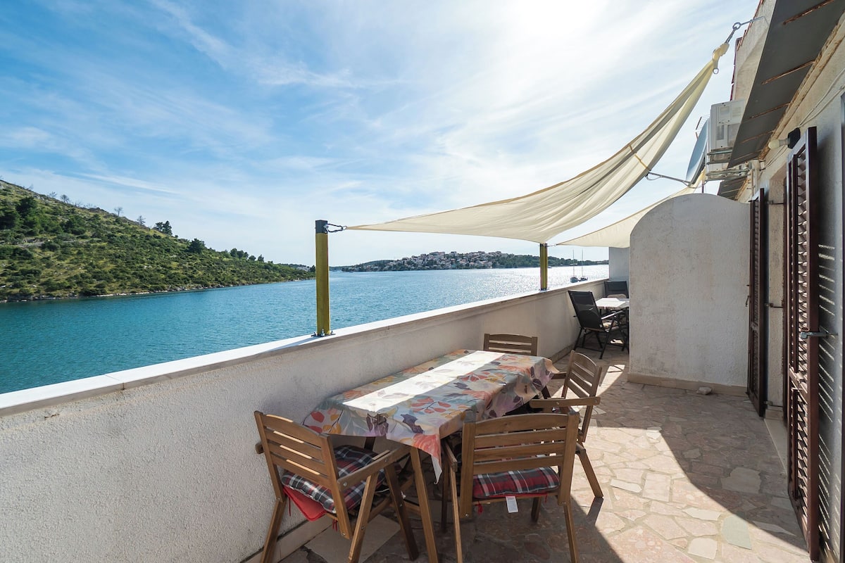 A terrace with a table and chairs, overlooking a body of water and a hillside.