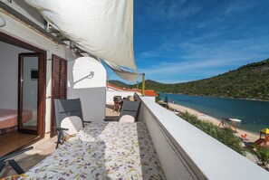 A balcony with a bed, a table, and a view of the beach and sea.