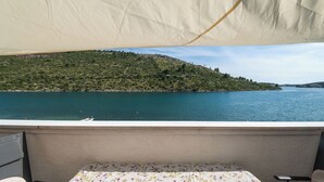 A balcony with a table and chairs, overlooking a lake and a green hillside.