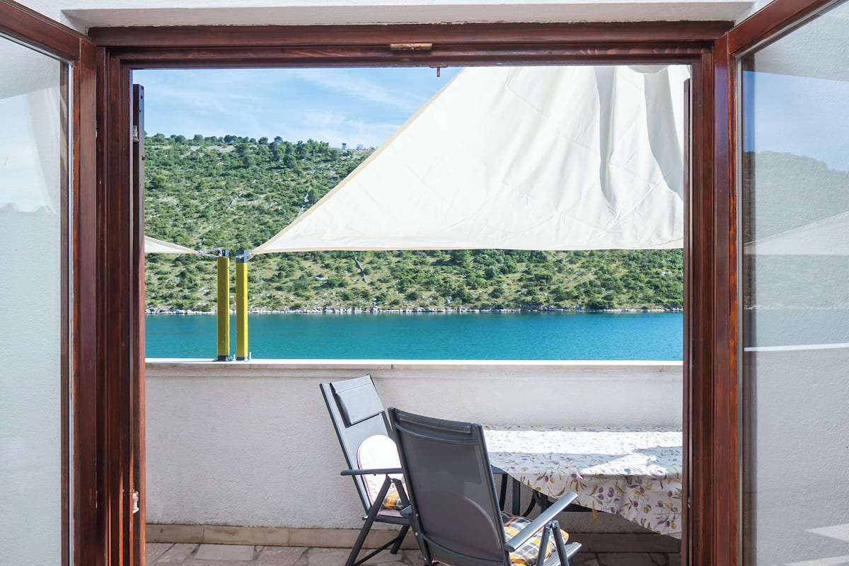 A balcony with a table and chairs, overlooking a lake and green hills.