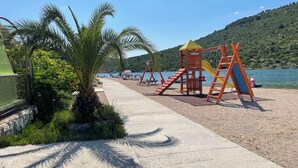 A playground with slides and climbing structures near a body of water, surrounded by greenery and a clear sky.