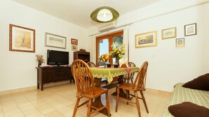 A dining area with a table set for four, surrounded by wooden chairs, a television on a cabinet, and framed pictures on the walls. - Apartments Luna Gordana (Razanj)
