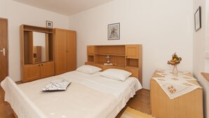 A bedroom with a bed, wooden wardrobe, and a bedside table with a vase. - Apartments Luna Gordana (Razanj)