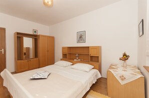 Een slaapkamer met een bed, een houten garderobe en een nachtkastje met een vaas.