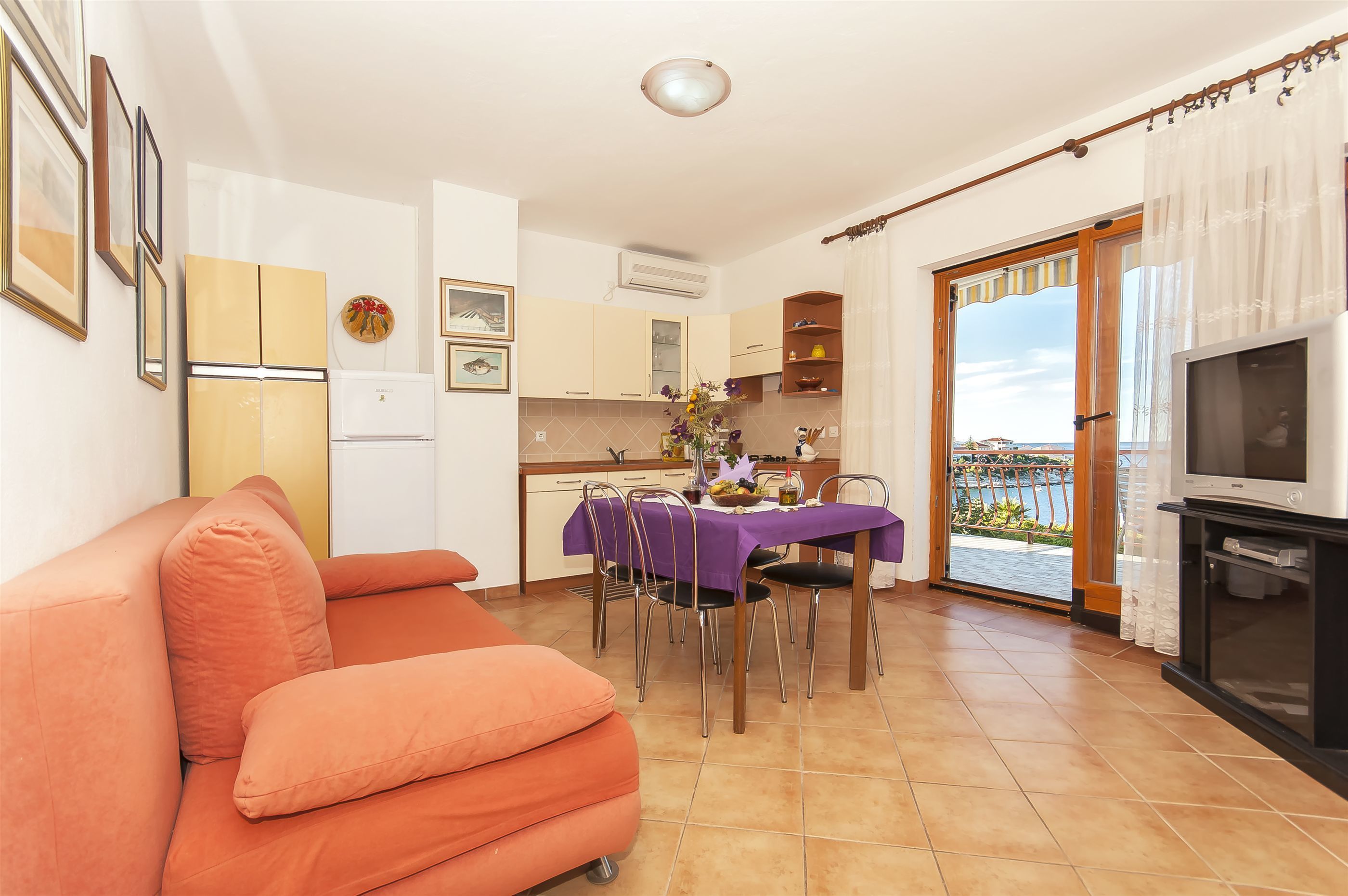 A compact living space with a sofa, dining table, kitchen, and a balcony with a view.