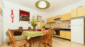 A compact kitchen with yellow cabinets, a white refrigerator, and a dining area with two wooden chairs and a table. - Apartments Luna Gordana (Razanj)