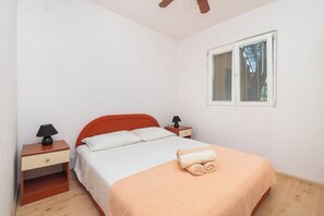 Un dormitorio con una cama individual, una mesita de noche con lámpara, una ventana con persianas y un ventilador de techo.