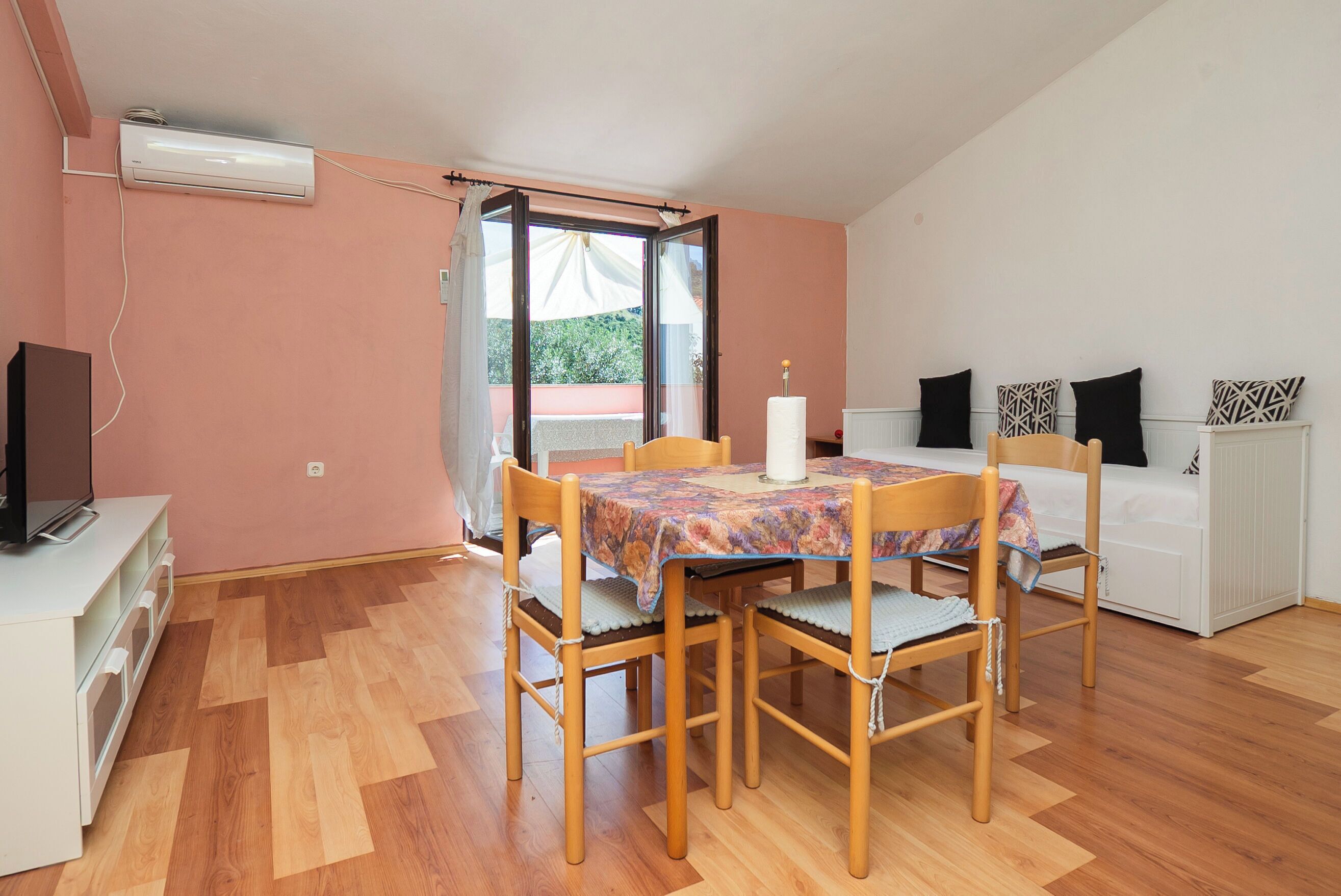 A room with a dining table, chairs, a TV, and a sofa.