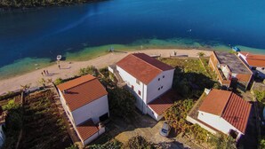 A coastal village with white buildings and red roofs, a clear blue sea, and a hilly backdrop.