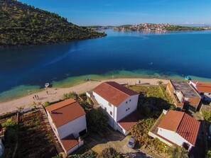 A coastal village with white buildings, clear blue waters, and a hilly backdrop.