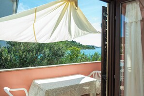 A balcony with a table and chairs, a white canopy, and a view of greenery and water.