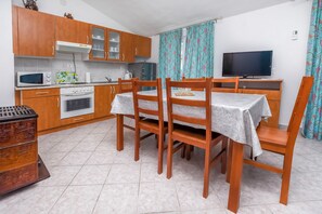 Une cuisine compacte avec des meubles en bois, un four à micro-ondes, un grille-pain et une cuisinière. On y trouve une table à manger avec des chaises et un téléviseur posé sur un meuble.