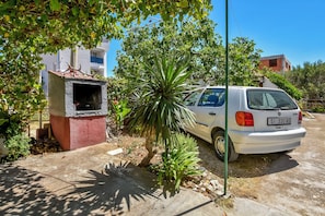 A white car parked in a driveway, a concrete structure with a small opening, and a palm tree. - Apartments Jelka (Rogoznica)