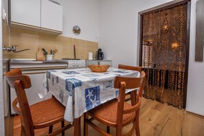 Uma cozinha compacta com uma mesa posta para dois, cadeiras de madeira e uma cesta decorativa.