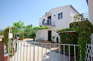 A white two-story house with a balcony, a gated entrance, and potted plants.