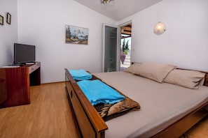 A bedroom with a bed, a TV on a wooden cabinet, a painting on the wall, and a balcony door.