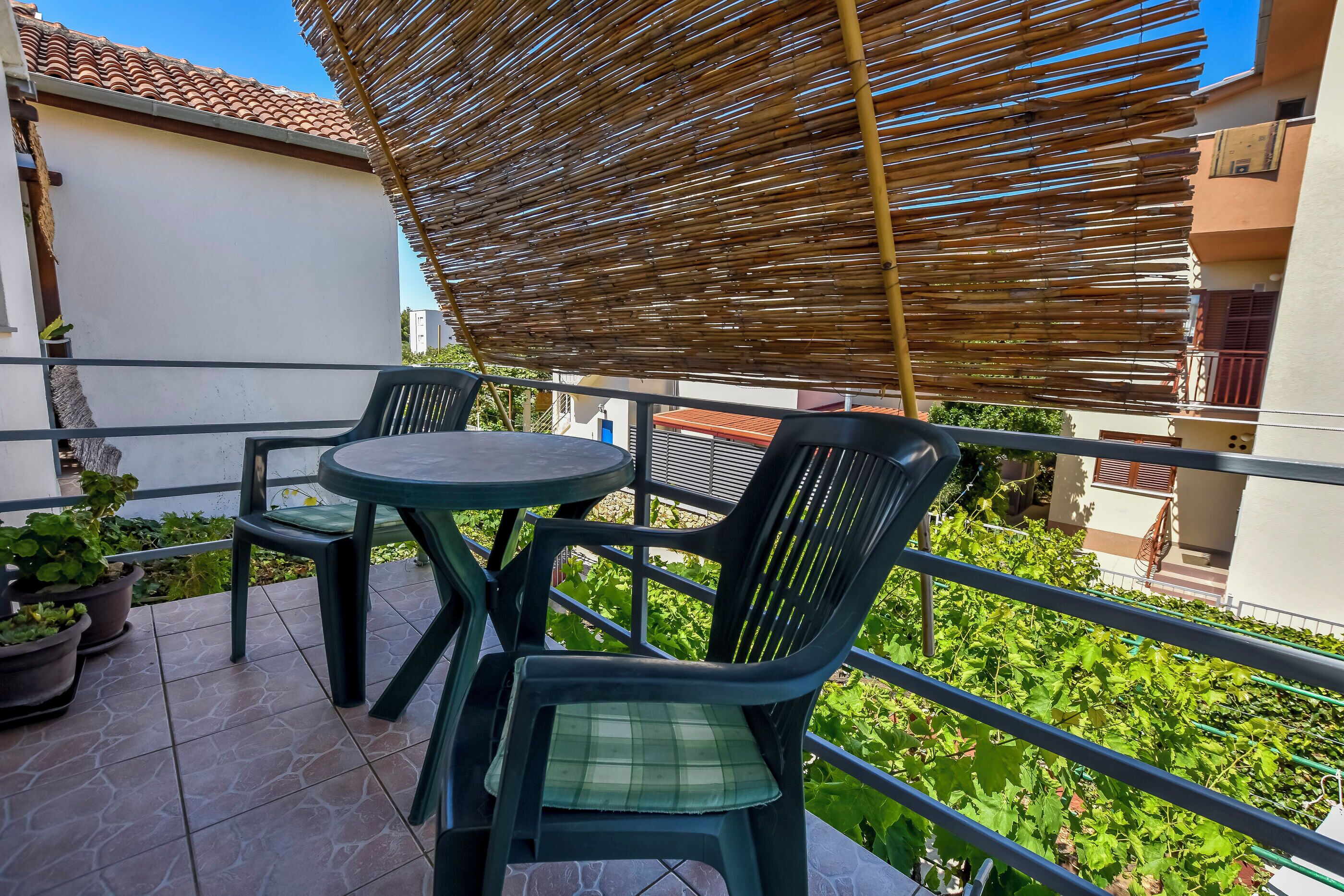 Een balkon met twee stoelen, een tafel, een bamboe zonnescherm en potplanten.