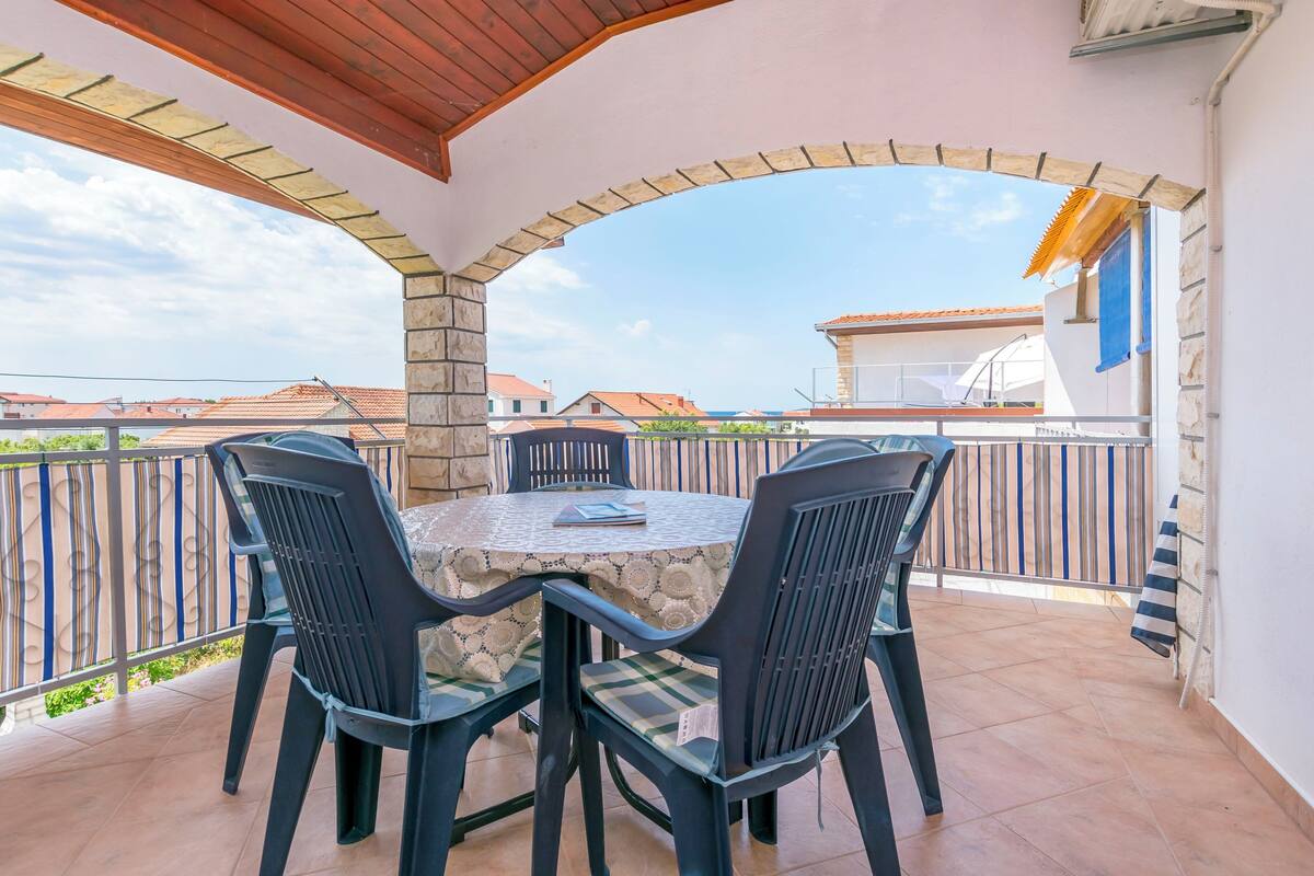 A covered outdoor patio with a stone table and four chairs, a view of neighboring houses, and a railing.