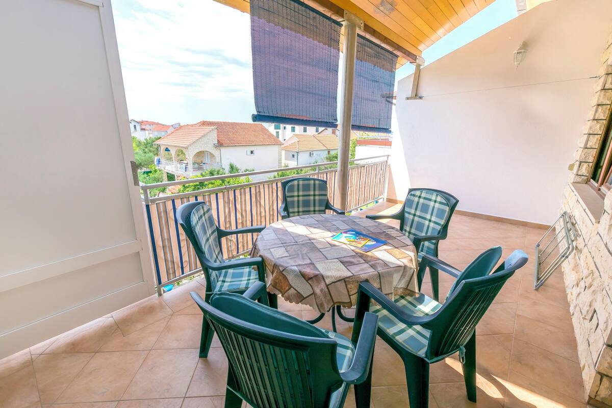 A balcony with a table and chairs, a view of houses, and a stone wall.