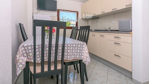 A small kitchen with a dining table and chairs, a TV mounted on the wall, and a window with a curtain.