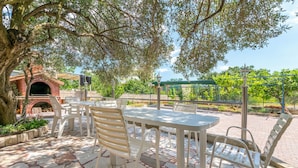 An outdoor patio with a brick oven, white plastic chairs, and a table.