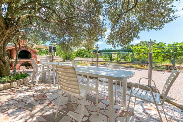 An outdoor patio with a brick oven, white plastic chairs, and a table.