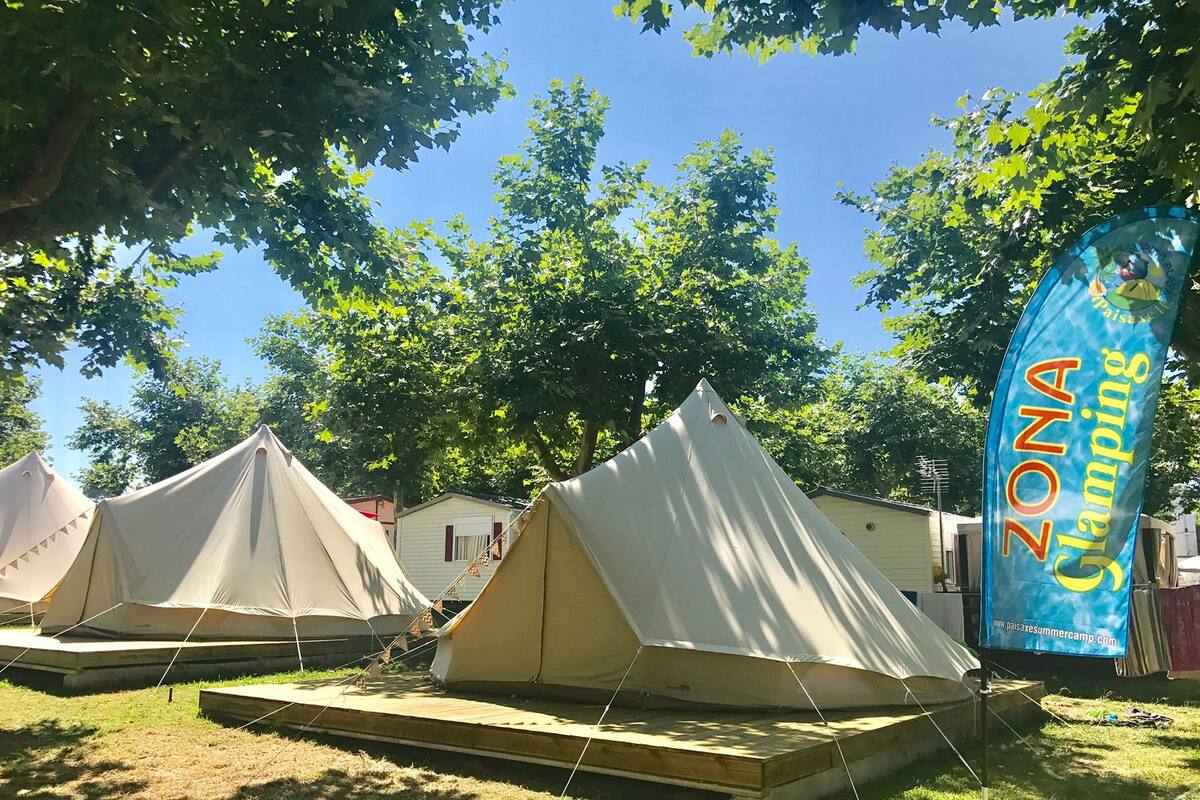 A campsite with multiple tents, a flag, and a small building in the background.
