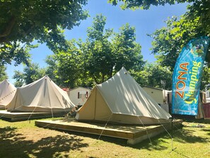 A campsite with multiple tents, a flag, and a small building in the background. - Camping Paisaxe II (O Grove)