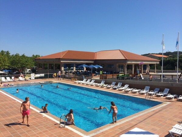 A swimming pool area with lounge chairs and a building in the background. - Camping Paisaxe II (O Grove)
