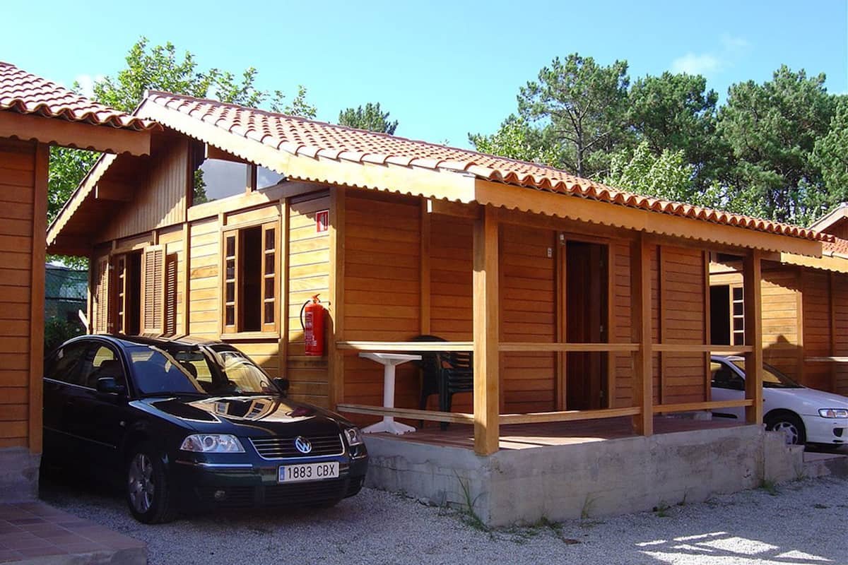 A wooden cabin with a tiled roof, a fire extinguisher, and a table outside.