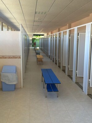 A corridor with rows of single rooms, a trash bin, and a row of blue tables. - Camping Paisaxe II (O Grove)