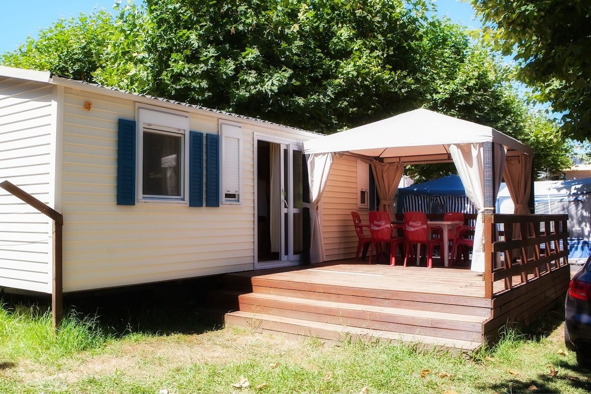 A mobile home with a porch, red chairs, and a covered seating area.