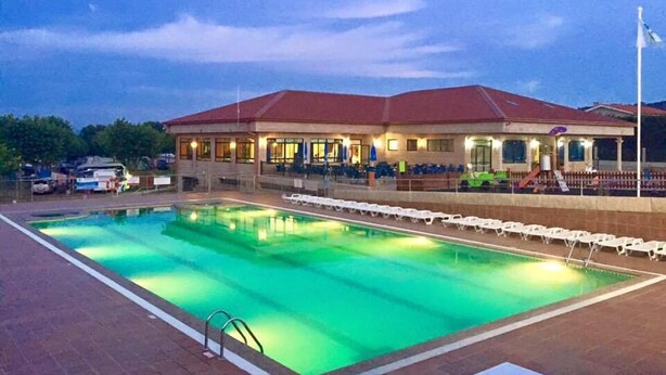 Uma piscina com espreguiçadeiras e um edifício com telhado vermelho ao fundo.