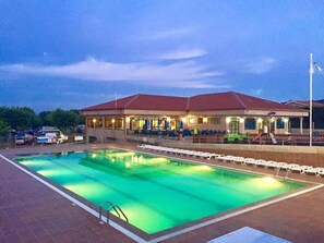 A swimming pool with lounge chairs and a building with a red roof in the background. - Camping Paisaxe II (O Grove)