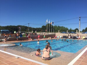 A swimming pool with people enjoying the water, a lifeguard tower, and flags in the background. - Camping Paisaxe II (O Grove)