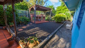Un espace barbecue extérieur abrité, doté d’un sol en pierre, entouré de plantes en pot et d’une clôture.