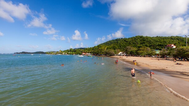 Une plage avec une eau cristalline, des gens qui se baignent et une rive sablonneuse.