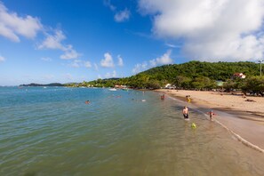 A beach with clear water, people swimming and walking along the shore, and a hill with trees in the background. - Eclats de Mer, 3 Waterfront Bungalows in Tartane / WIFI Car Rental (Tartane, Trinité)