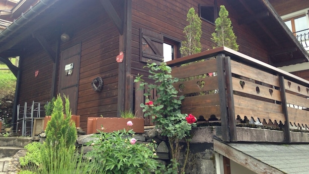 Une cabane en bois dotée d’une véranda, d’un escalier en pierre et d’une clôture en bois ornée de découpes en forme de cœur.