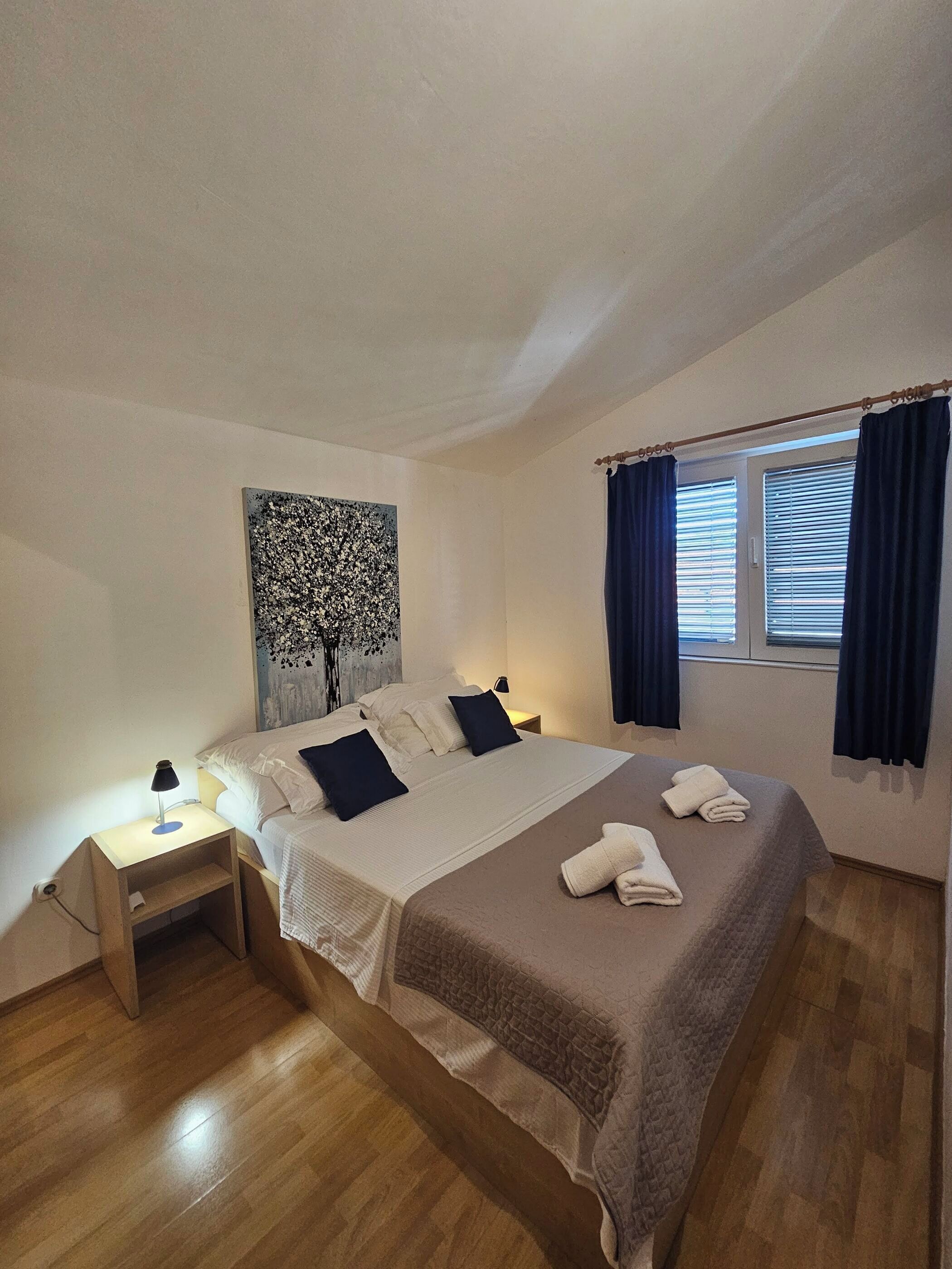 A neatly arranged bedroom with a bed, bedside table, and a window with curtains.