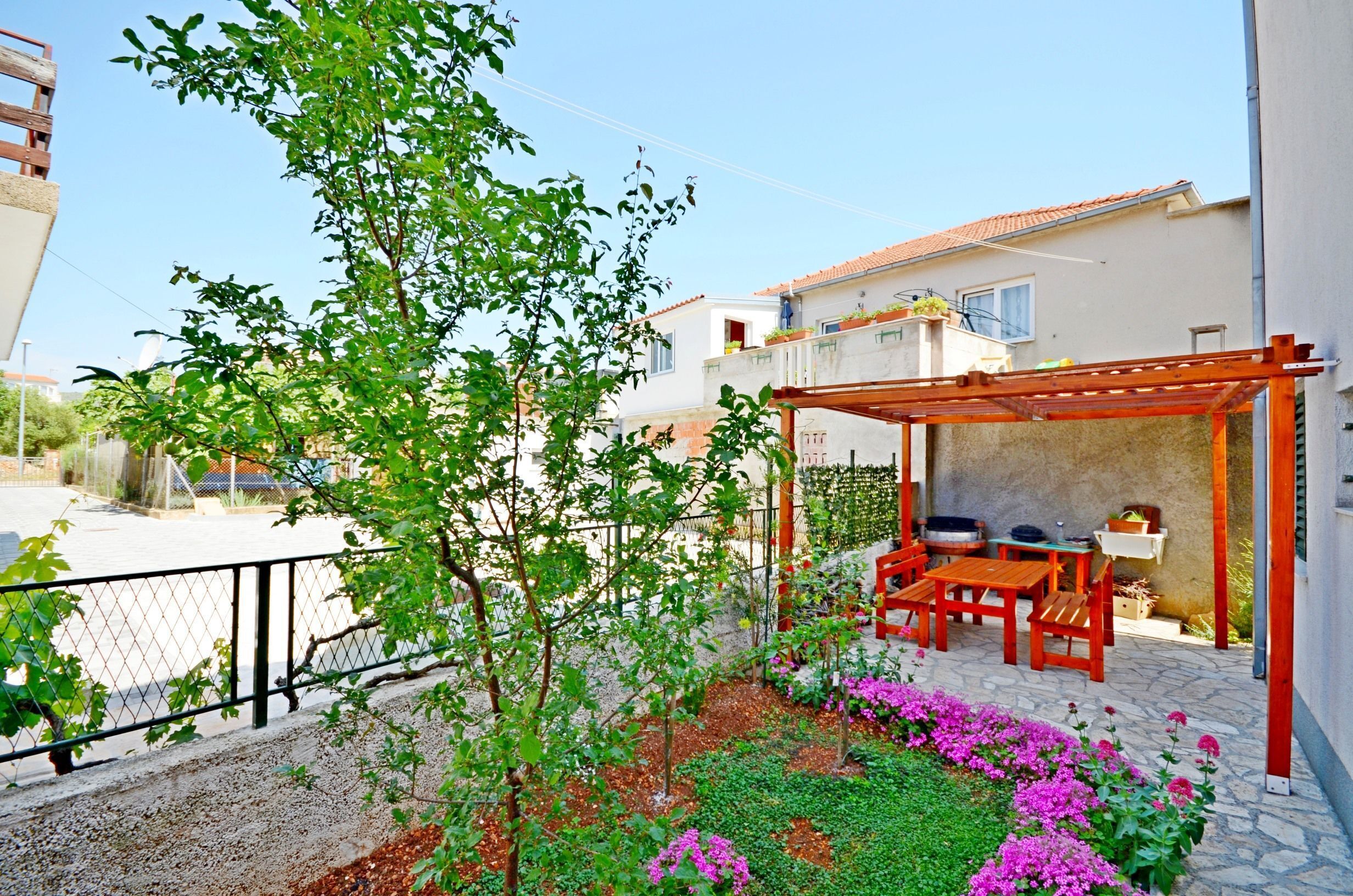 A patio with a wooden pergola, outdoor seating, and a garden with flowers.