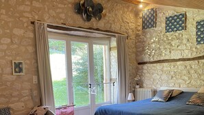 Una habitación con dos camas, paredes de piedra, techo de madera y un ventanal con cortinas.