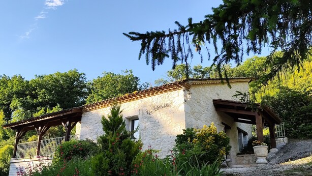 Un rústico edificio de piedra con una pérgola de madera y una escalera de piedra que conduce a la entrada.