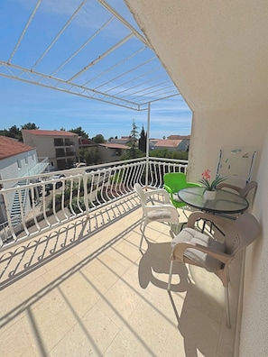 A balcony with a white railing, a glass table, and plastic chairs.