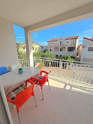 A balcony with a table and chairs, a view of neighboring buildings, and a clear sky.