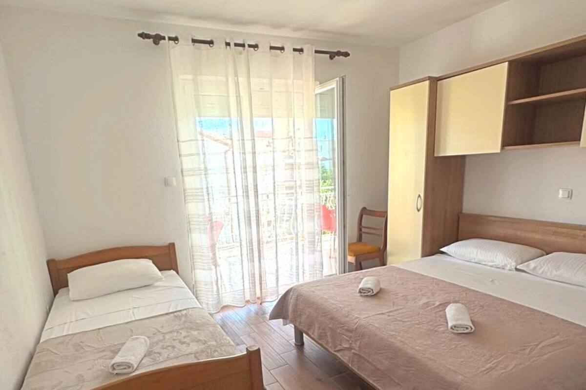 Una habitación con dos camas, cabecero de madera, una silla de madera y una puerta corrediza de vidrio.