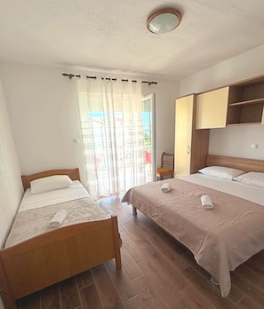 A room with two beds, a wooden headboard, a wooden chair, and a sliding glass door.