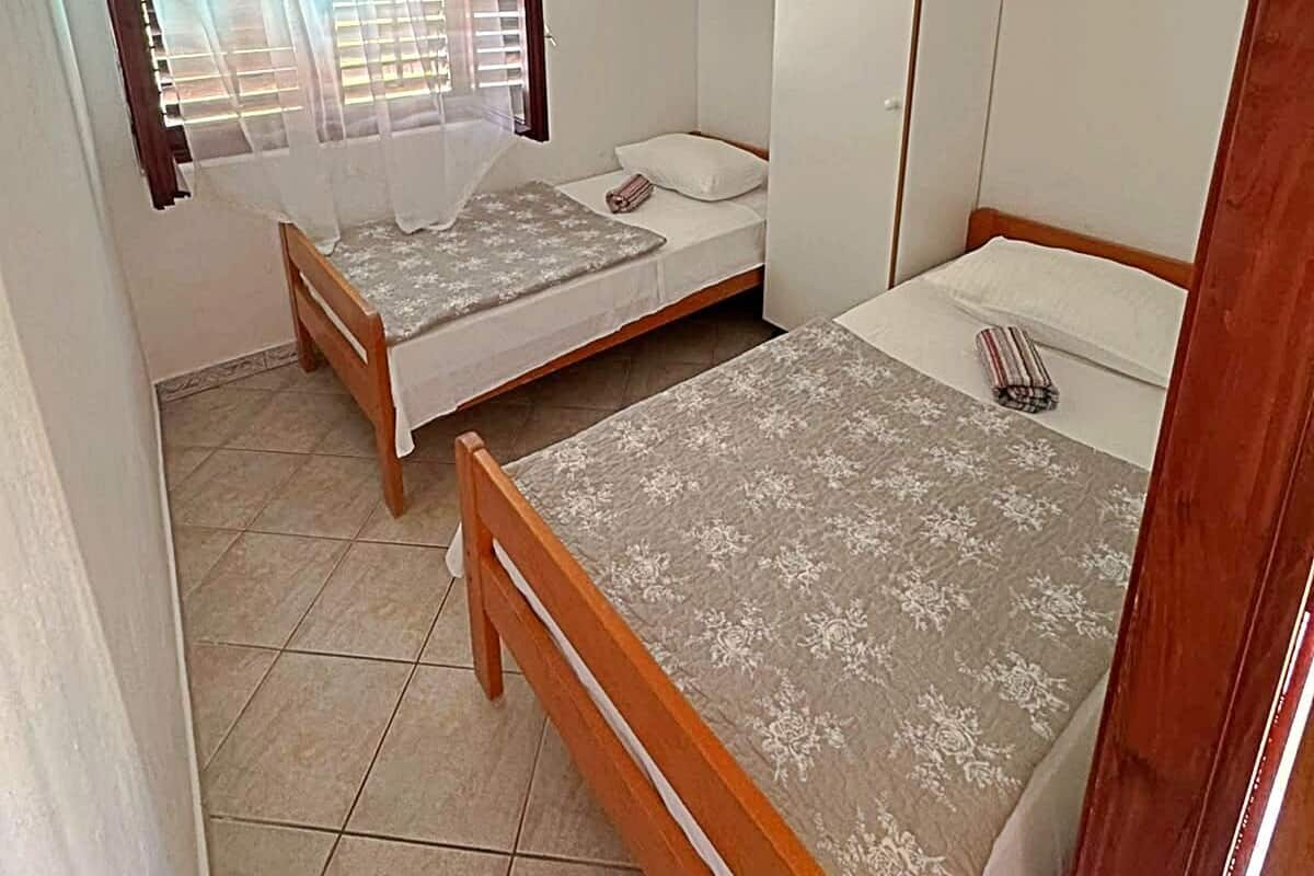 Un alojamiento pequeño, de una sola habitación, con dos camas, una ventana con cortinas, un armario y suelo de baldosas.