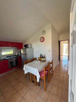 A compact kitchen with red cabinets, a microwave, a stove, and a dining table set for two with chairs.
