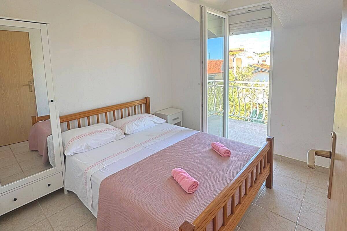 Un dormitorio con cama, espejo, puerta corredera a un balcón y una mesita.